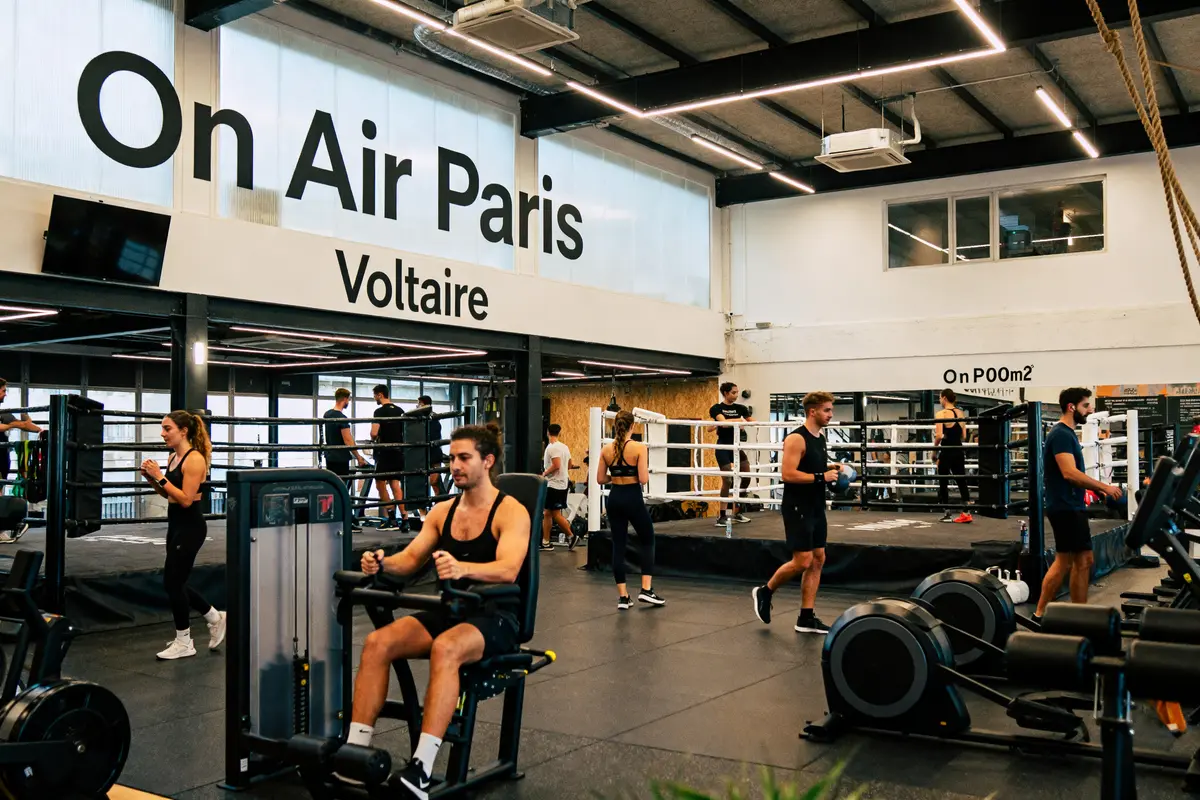 Salle de sport On Air Paris, personnes s'entraînant avec équipements et ring de boxe en arrière-plan.