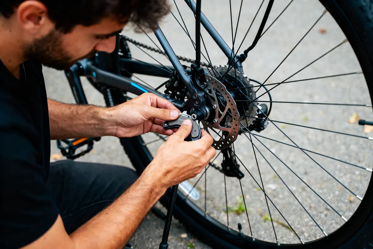 Homme répare frein à disque sur roue arrière de vélo, en extérieur.