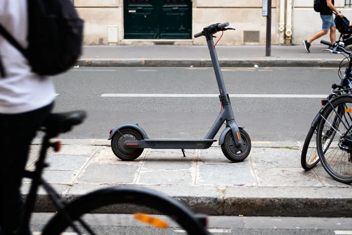 Trottinette électrique garée sur un trottoir, cycliste flou au premier plan, rue urbaine.