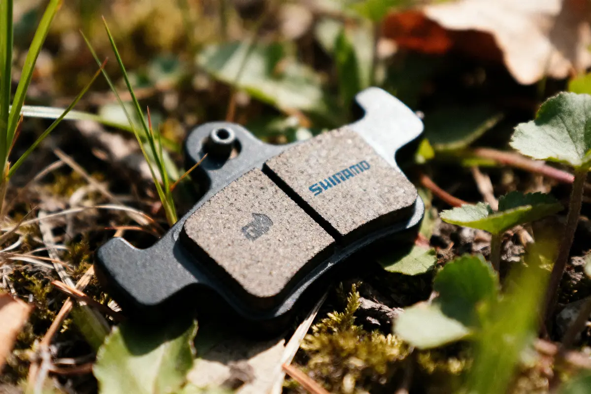 Plaquette de frein Shimano sur sol herbeux avec feuillage environnant en arrière-plan.