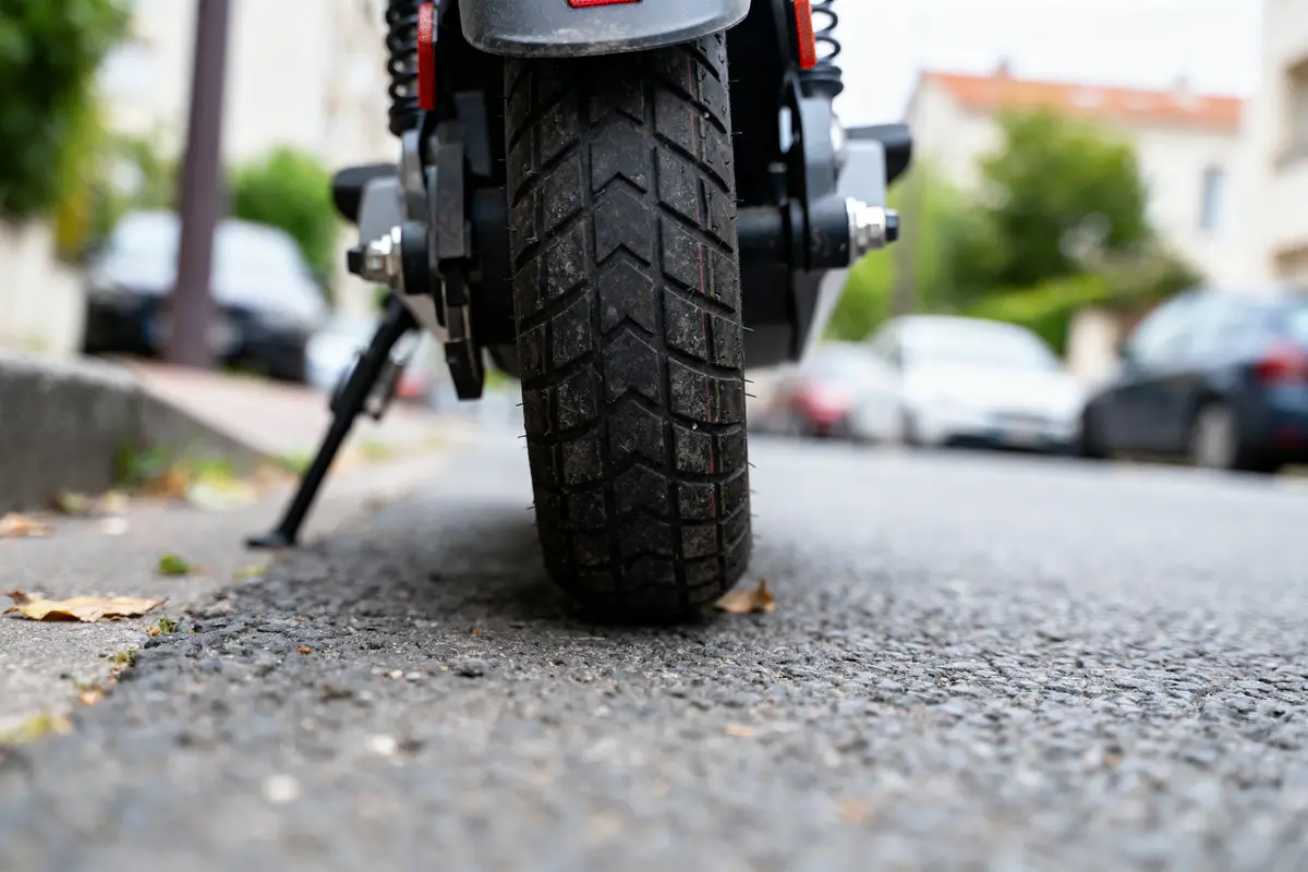 Vue rapprochée d'une roue arrière de scooter sur une route urbaine, voitures floues en arrière-plan.